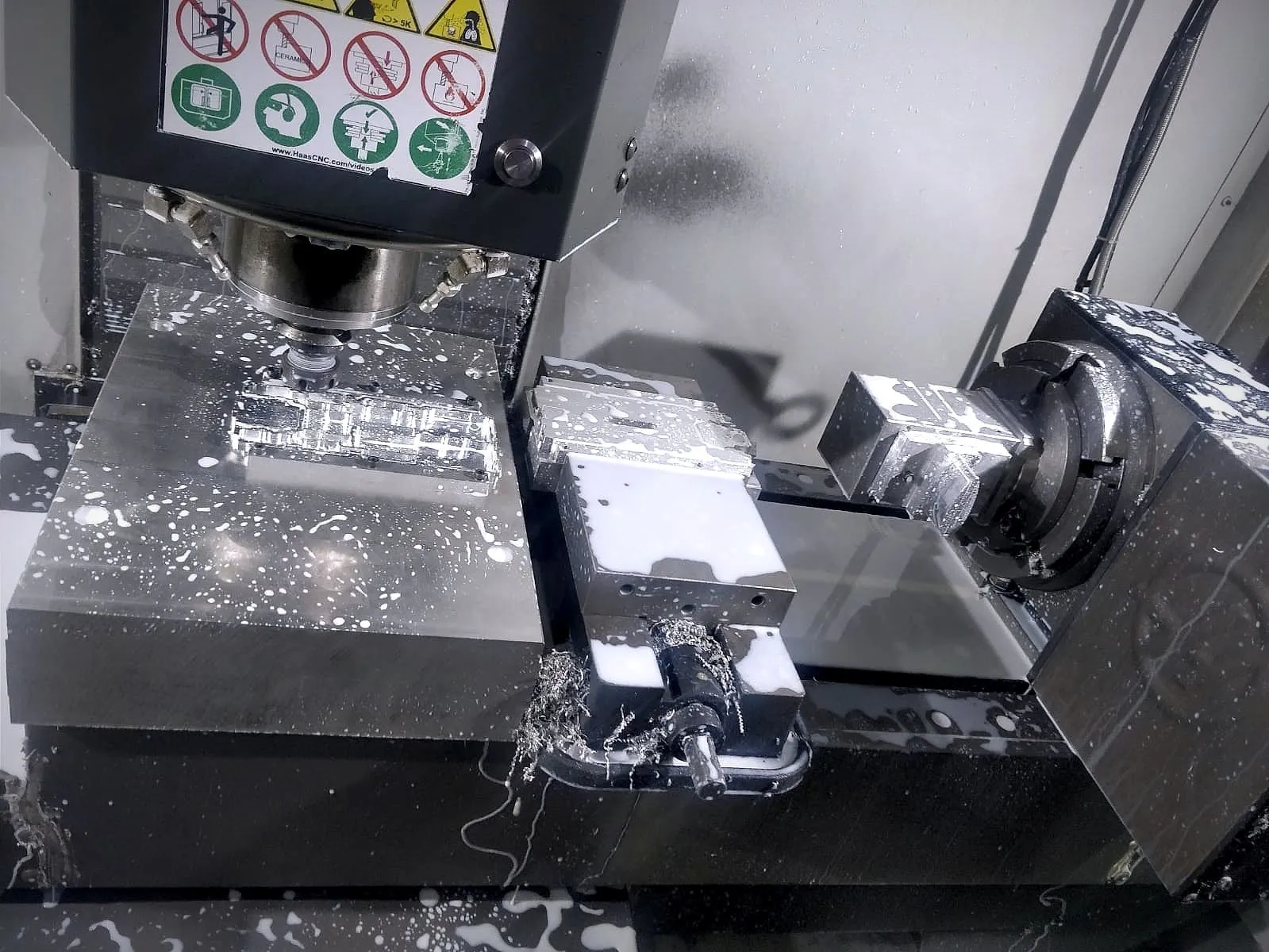 Part being machined in a vertical machining centre, with a vise and rotary table